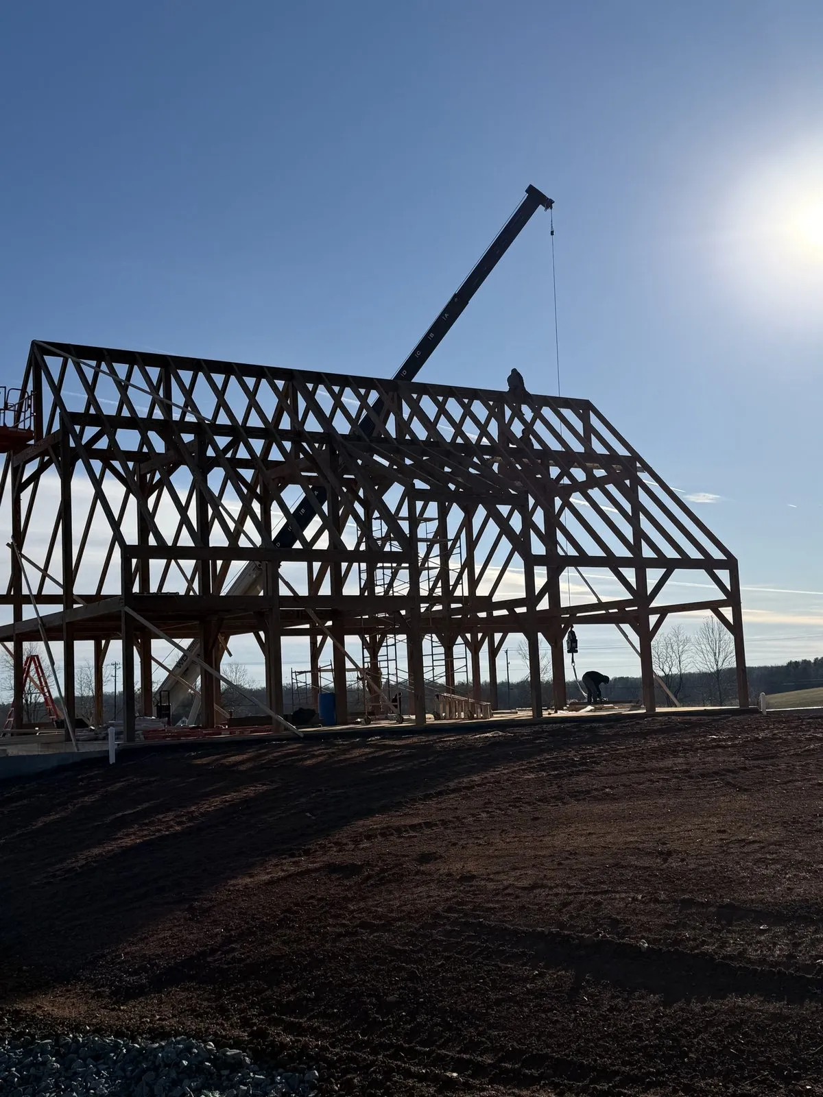 Timber frame raising in progress on a Virginia design-build project site with crane and crew